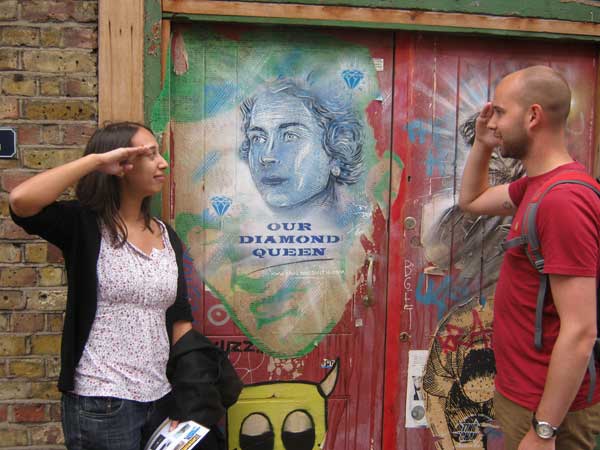Team members saluting a portrait of the Queen on a Spitalfields wall.